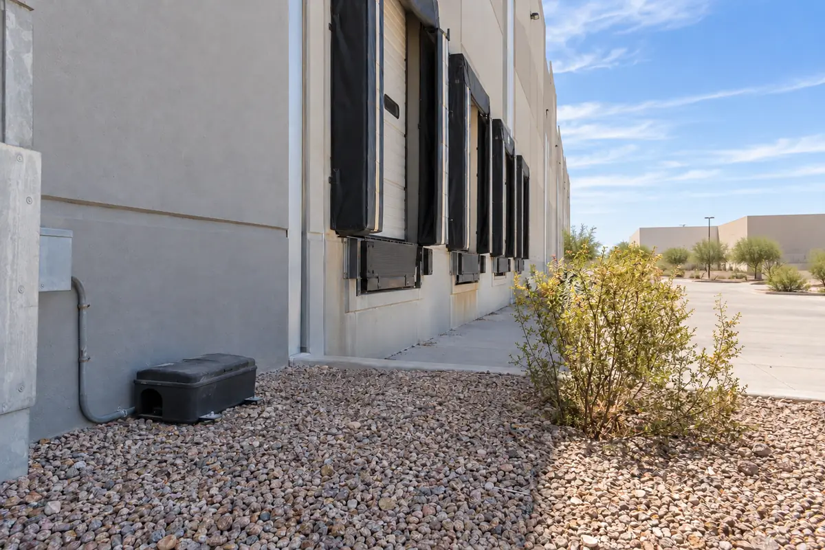 Loading dock doors at a commercial building with a bait station on the gravel, commercial pest control in Allen, TX
